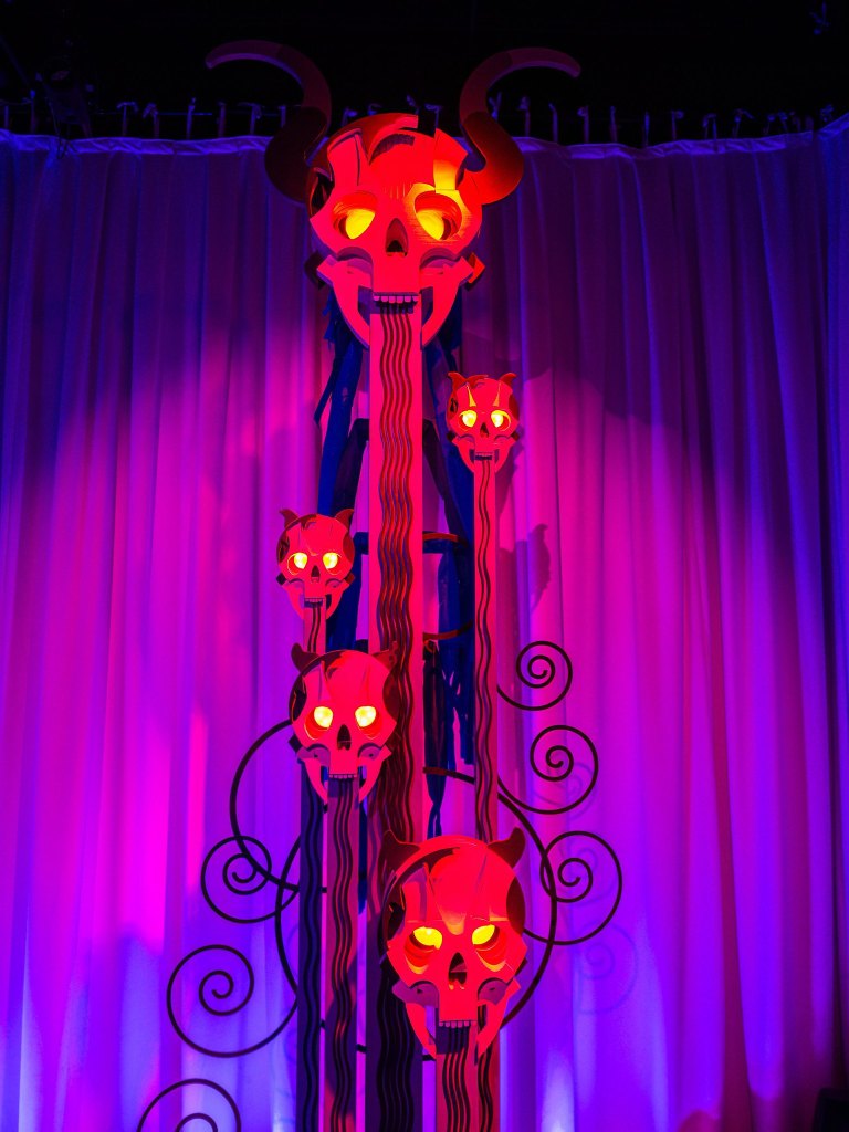 A vertically arranged decorative structure featuring red and orange glowing skulls, accompanied by dark swirling designs, against a purple-lit backdrop.