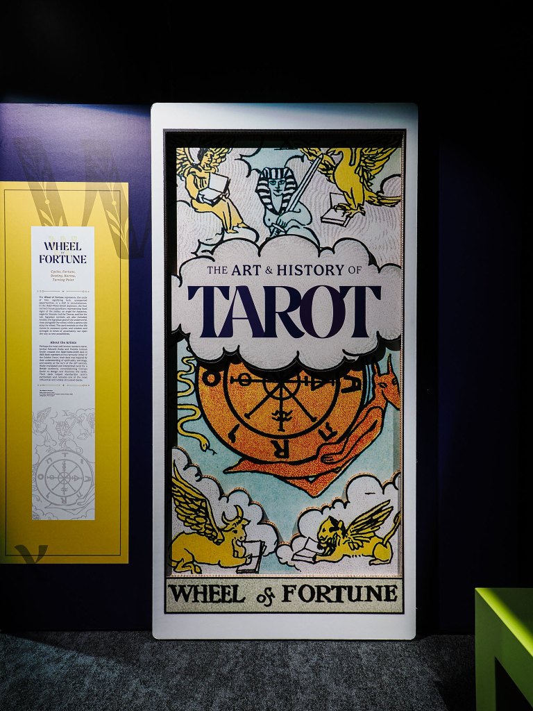 Exhibition display featuring the 'Wheel of Fortune' tarot card and text about the art and history of tarot.