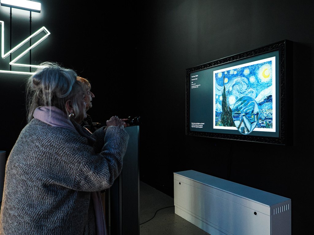 Two people viewing a digital display of Vincent van Gogh's 'Starry Night' in an art exhibit.