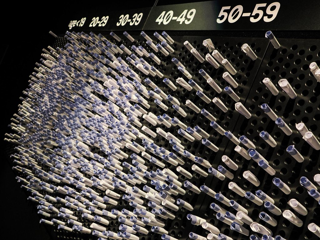 An abstract display made of numerous white and blue tubes arranged on a black background, categorized by age groups from under 19 to 50-59.