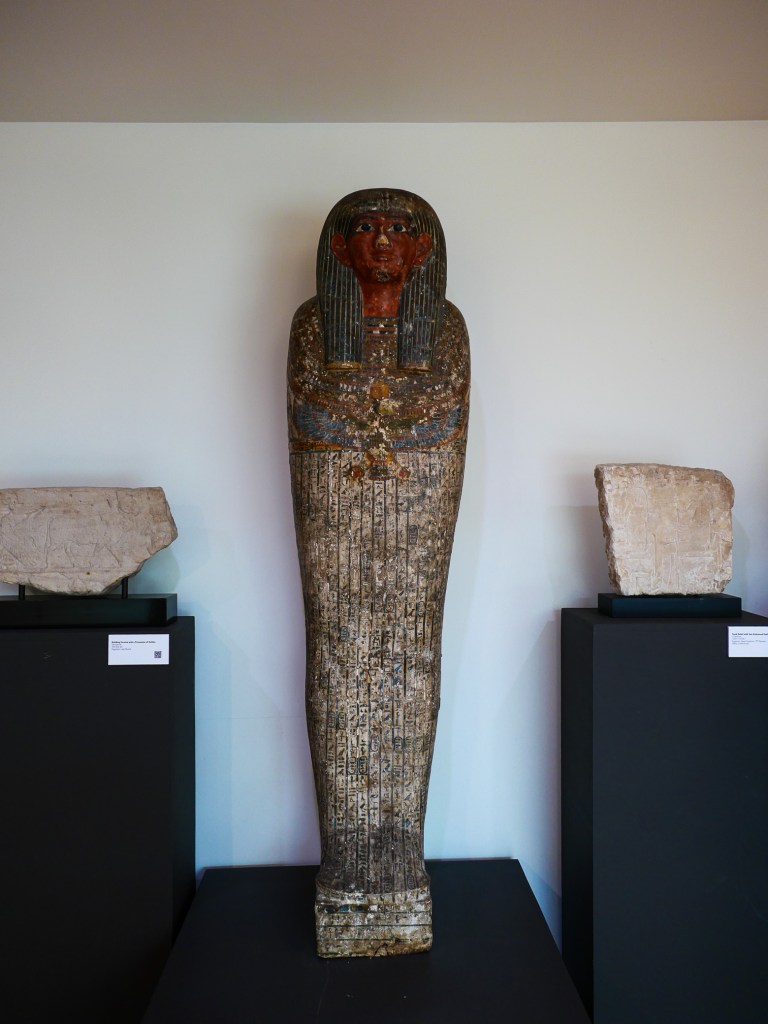 Ancient Egyptian coffin figure with intricate carvings and painted features, displayed in a museum setting.