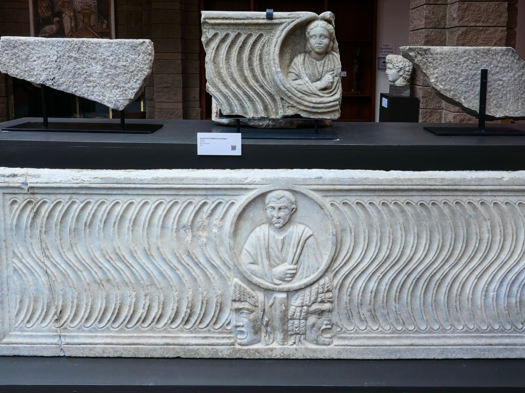A display of ancient stone artifacts featuring carvings, including a relief depicting a figure in a circular frame, surrounded by wavy patterns and additional stone fragments.