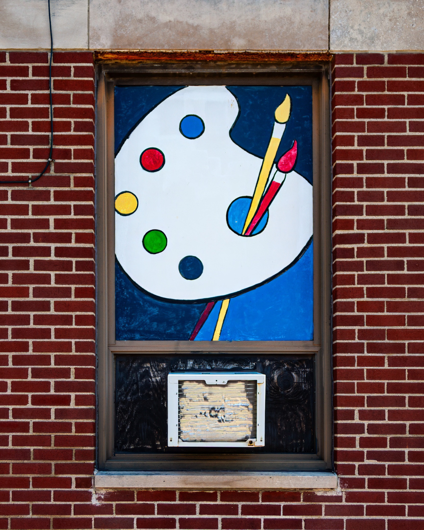 A painted window feature showing an artist's palette with colorful paint spots and brushes, set against a blue background, framed by a brick wall.
